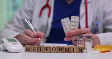 Doktor metformin için reçeteli reçete hazırlıyor ve elinde hasta için tabletler tutuyor. Masa üzerindeki minyatür tahta bloklar. İlaç adı: