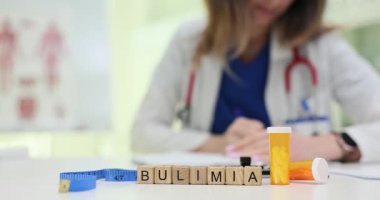 Doktor ölçüm bandına yakın raporlar yazarken, tahta küpler masa büyüsü kelimesinde Bulimia yazıyor. Hap şişesi hastalar için yeme bozukluğu terapisini ön plana çıkarır