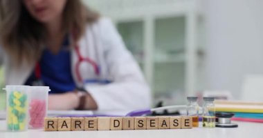 Doktor masasında steteskop tüpleri ve kapsüllerle nadir rastlanan bir hastalık ifadesi var. Kadın hekim çalışmaları hastanede rapor veriyor.