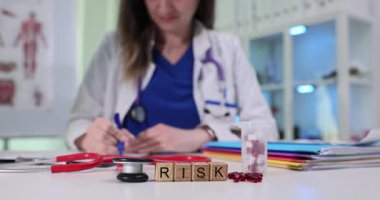 Tahta küplerin hecelenmesi, kapsüllerin yanında risk ve tıbbi kararın şişesi anlamına gelir. Kadın doktor hasta değerlendirmesi sırasında yavaş çekimde notlar yazar.