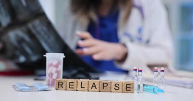 Tahta küpler, doktor masasında dağınık haplar ve şişelerle kelimenin nüksetmesi anlamına gelir. Beyaz önlüklü kadın doktor modern klinikte röntgen üzerinde çalışıyor.