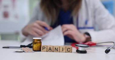 Doktor hastanın tıbbi geçmişini gözden geçirir ve panikle başa çıkmak için detaylı tavsiyeler yazar. Küçük tahta küpler masada paniğe yol açar.