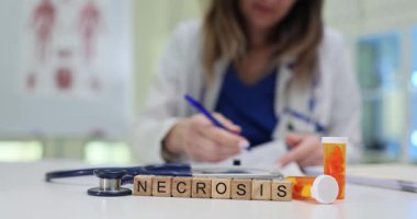 Doktor nekroz için tedavi önerilerini dikkatlice yazıyor. Masa başı teriminde tahta küpler steteskop ve hapların yanında nekroz.