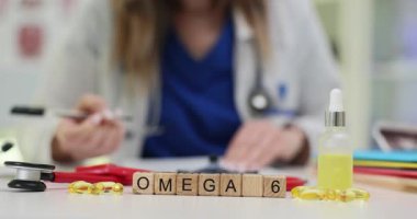 Kadın doktor vitamin alımı için detaylı tavsiyeler yazar. Küçük tahta bloklar, kapsüllerin yanında Omega 6 terimi ve masa üzerinde stetoskop oluşturur.