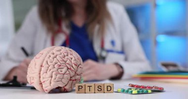 Kadın hekim hasta çizelgesinde tedavinin aşamalarını özetliyor. Masanın üzerindeki beyin modelinin yanında, tahta bloklar TSSB kısaltması şeklinde düzenlenmiş.