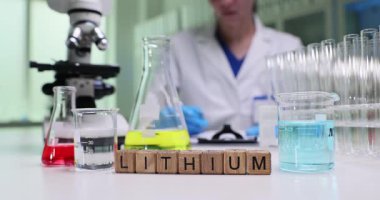 Kadın kimyager lityum analizinin sonuçlarını dikkatlice yazar. Tahta bloklar düzgünce düzenlenmiş laboratuvar ekipmanlarının yanında lityum sözcüğü oluşturuyor.