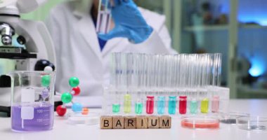 Kadın kimyager, soluk sıvıyı mikroskopla test tüpünde dikkatlice inceliyor. Sözcük baryumu oluşturan tahta bloklar araştırma konusunu vurguluyor