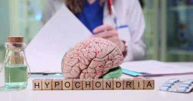 Psikiyatrist, hastanın uzun süredir devam eden semptomlara yakından baktığı tıbbi geçmişi inceliyor. Tahta bloklar masadaki hipokondriyi oluşturur.