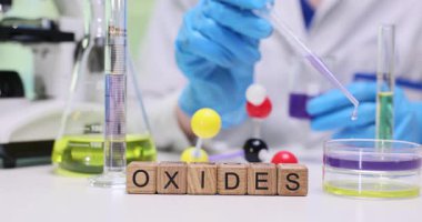 Laboratuvar asistanı canlı mor sıvıyı petri kabına aktarmak için pipette kullanır. Tahta küpler düzenlenmiş form kelime oksitler çalışma altında konu göstermektedir