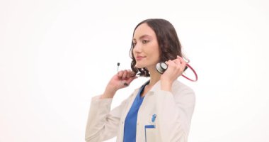 Beyaz önlüklü kadın doktor steteskopu boynuna doğru kaldırıyor. Doktor, klinikte ağır çekimde vardiyaya hazırlanırken steteskop kulaklığı takıyor.