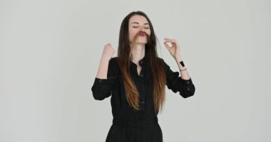 Uzun saçlı genç bir kadın, ipliği şakacı bir bıyık gibi kaldırıyor. Ağır çekimde kadınlar stüdyoda komik bir ifade takınıyor.