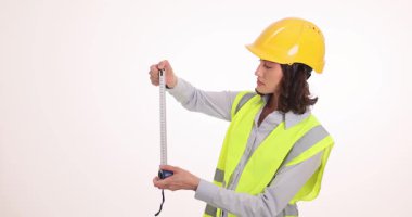 Güvenlik yeleği giyen kadın mühendisin elinde uzun bir mezura var. Projede yavaş çekimde ölçeği dikkatle incelerken, inşaatçı uzunluk okumasını kontrol eder