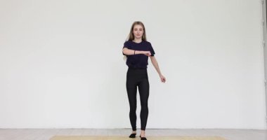 Koyu renk tişörtlü genç bayan küçük hamlelerle öne çıkıyor. Kadın kollarını ritmik olarak hareket ettiriyor stüdyo ağır çekimde basit kardiyo dansı egzersizleri yapıyor.