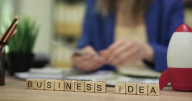 Ofis masasındaki ahşap bloklar iş fikirlerini paraya yakın hecelerler. İş kadını, roket oyuncağı planlama projesinin yakınındaki banknotları sayıyor