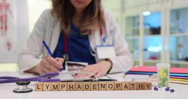 Stetoskop yakınındaki masa büyüsü kelime lenfadenopati üzerinde tahta bloklar. Kadın doktor, randevuda şişmiş düğümler hakkında yazılan resimleri tarar.