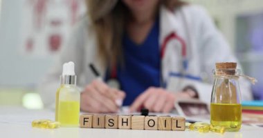 Balık yağını ahşap bloklara, sarı sıvı şişelerin ve klinikteki kapsüllerin yanına yaz. Doktor kadın hastanedeki hastaya ilave reçete yazıyor.