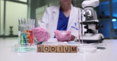 Sodyum, ahşap küplere ve masa üzerinde renkli sıvılara sahip camlara yazılır. Kadın bilim adamı, kimya laboratuvarında petri kabına toz koyan örnekleri analiz ediyor.