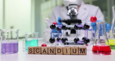 Laboratuvarda renk sıvıları ve moleküler yapı modelinin yakınındaki tahta bloklardan oluşan kelime çözeltisi. Kadın kimyager soruşturma sırasında mikroskoba bakar.