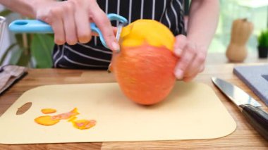 Mutfakta parlak balkabağının derisini yüzerken aynasızlar elinde tutuyor. Aşçı, sonbahar çorbası için plastik kesme tahtasındaki sebze yüzeyini temizler.