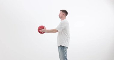 Günlük kıyafetli bir adam basketbol topunu açık elle havaya fırlatıyor. Atletik oyuncu top denetimi yapıyor. Basit alıştırma egzersizlerinin tadını yavaş çekimde çıkarıyor.