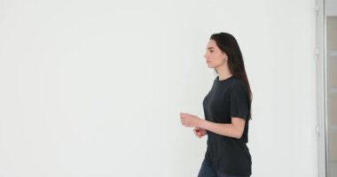 Siyah tişörtlü ve atletik pantolonlu bir kadın geniş oturma odasında hafif hafif koşuyor. Gevşek saçlı bir kadın yaklaşan antrenman için ısınıyor. Yavaş çekim