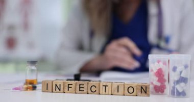 Tahta bloklar kelime enfeksiyonunu ilaç kutusuyla birlikte ilaç şişesinin yanında hecelerler. Kadın doktor enfeksiyon riski faktörleri üzerine notlar yazıyor.