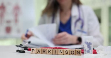 Tahta bloklar steteskop ve kağıtların önünde Parkinson kelimesini heceler. Kadın doktor hareket bozukluğu risklerini tartışan nöroloji raporu yazdı