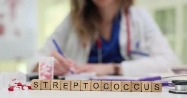 Tahta bloklar, kapsül kapsüllerinin yanında Streptococcus kelimesi ve masanın üzerindeki çizelge. Kadın doktor, bakteriyel boğaz enfeksiyonu üzerine rapor yazıyor.