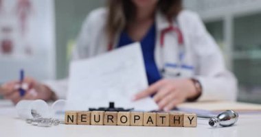 Tahta bloklar parlak steteskop yakınlarında nöropati kelimesini heceler. Kadın doktor sinir hasarı notları yazar. Hasta tablosunu dikkatlice kontrol eder.