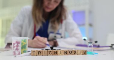 Tahta bloklar ilaç ve şırınganın yanında Trişinoz kelimesini heceler. Kadın doktor, kas semptomlarını izleyen parazit enfeksiyonu notları yazıyor.