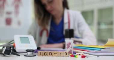 Tahta bloklar kod ICD 10. Kan basıncı monitörü ve stetoskop yakınında. Kadın doktor teşhis koduna giriyor. Hastanın tıbbi kayıtlarını düzenliyor.