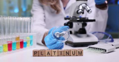 Tahta bloklar masa üzerinde cam test tüpleriyle platin sözcük kodlar. Paltolu bilim adamı, üzerinde mikroskop olan cam bir çanak tutuyor.