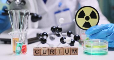 Laboratuvar kürsüsündeki tahta küpler uluslararası radyasyon sembolü yakınındaki Curium kelimesini heceliyor. Eldivenli bilim adamı atom modelini gözlemlemek için örnek test hazırlıyor