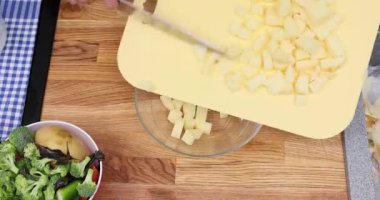 Tecrübeli şef taze kesilmiş patatesleri tahta kesme tahtasından şeffaf kaseye aktarıyor. Aşçı mutfakta patates rendelemek için rende kullanır.