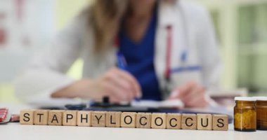 Kehribar şişeleri ve steteskopun yanında tahta bloklar var. Kadın doktor antibiyotik tedavisi planlayan enfeksiyon notları yazıyor.