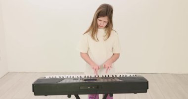 Elektronik klavyenin başında duran genç kız piyano tuşlarına basıyor. Çocuk müzisyen notaları dikkatli bir ritimle tekrarlarken basit melodileri çalışır.