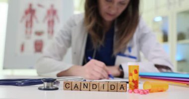 Tahta küpler düzgün bir şekilde yerleştirilmiş tanımlanmış mantar durumunu vurguluyor. Kadın doktor, hastanın dozaj detaylarına yoğunlaşması için reçete yazıyor.