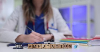 Steteskop yakınındaki tahta küplerde kelime ampütasyonu ve doktor masasında şırınga. Kadın cerrah, hastanedeki hasta ameliyatı için gerekli belgeleri hazırlıyor.