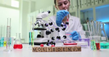 Laboratuvar teknisyeni kırmızı sıvıyı petri kabına koymak için pipet kullanıyor. Tahta harf blokları analizin odak noktasını tanımlayan kelime Molybdenum 'u oluşturur