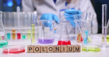 Kimyager, sıvının rengini ve berraklığını gözlemlemek için test tüpünü eğiyor. Tahta küpler Polonyum sözcüğünü oluşturur. Soruşturma altındaki maddeyi açıkça gösterir.