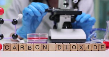 Kadın araştırmacı materyali modern mikroskop altında yakından inceliyor. Moleküler model karbon dioksit terimine dayalı minyatür ahşap harf küpleri