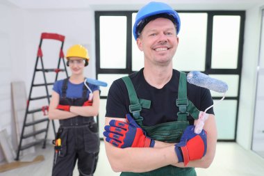 İki neşeli işçi, yeni yenilenmiş bir alanda, boya silindirleriyle harekete geçmeye hazır bir şekilde güvenle duruyorlar. Parlak üniformaları ve araçları projeye olan bağlılıklarını yansıtıyor..