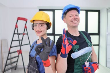 Neşeli gülümsemeleri olan iki yetenekli işçi ferah bir odada birlikte poz vererek yenileme projesine olan ilgilerini gösteriyorlar. Güvenlik kıyafeti giyiyorlar ve çalışmaya hazırlar..