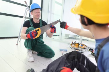 İyi ışıklandırılmış, çağdaş bir odada, iki adam bir inşaat projesiyle meşgul oluyor. Bir adam elinde testereyle diz çöker, diğeri de ona bir alet verir. Hem odaklanma hem de takım çalışması.