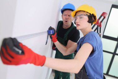 İki inşaat işçisi bir duvarı ölçmek için işbirliği yapıyor..