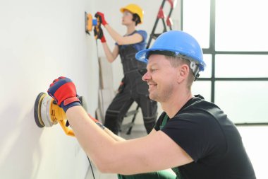 Çalışkan iki kişi modern bir binanın içini geliştirmeye odaklanıyor. Biri, doğal ışıkla dolu geniş bir ortamda aletleri hazırlarken diğeri özenle bir duvarı kumlar..