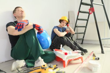 İşçiler duvarın önünde oturup, tadilatın ortasında dinleniyorlar. Boya ve onarımlarla dolu yoğun bir günde yakınlardaki araçlar ipucu dağıtıyor..