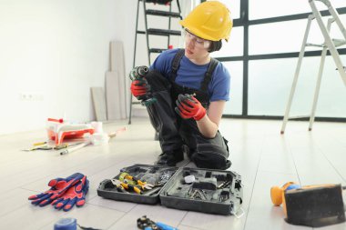 Kendini işine adamış bir işçi, açık bir alet çantasından araçları dikkatlice ayırarak yerde diz çökerken, aynı zamanda şık bir iç mekanda ev yenileme işine hazırlanıyor..