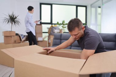 Geniş, güneşli bir dairede, bir adam büyük bir kutuyu hevesle açar ve içindekileri gösterir. Bir kadın yakınlarda duruyor, not defterine bir şeyler düzenliyor, yeni hayatlarına hazırlanıyor..