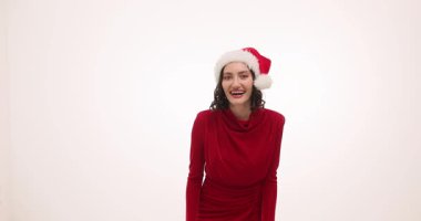 Parlak kırmızı elbise giyen Noel Baba şapkalı kadın yüksek sesle gülüyor. Mutlu model, stüdyoda Noel şakasının keyfini çıkarırken başını eğer ve ağır çekim yapar.
